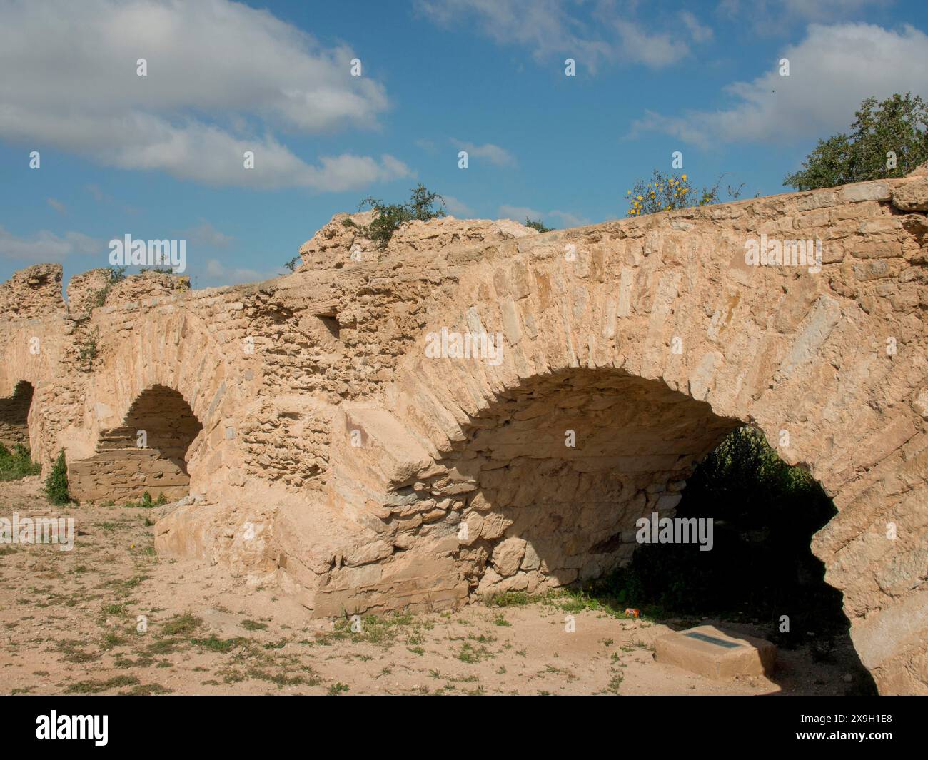 Enormi e antichi archi in pietra di una cinta muraria della città sotto un cielo azzurro chiaro testimoniano la storia del passato, Tunisi in Africa con rovine dell'epoca romana, moderna Foto Stock