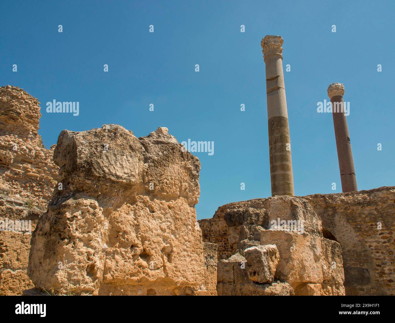 Antiche rovine con alte colonne e pietre sotto un cielo blu, Tunisi in Africa con rovine dell'epoca romana, moschee moderne e case bianche e blu Foto Stock