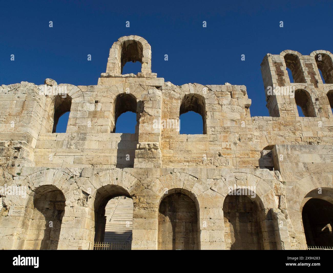 Antica struttura in pietra con archi multipli sotto un cielo azzurro, antichi edifici con colonne e alberi sull'Acropoli di Atene contro a. Foto Stock