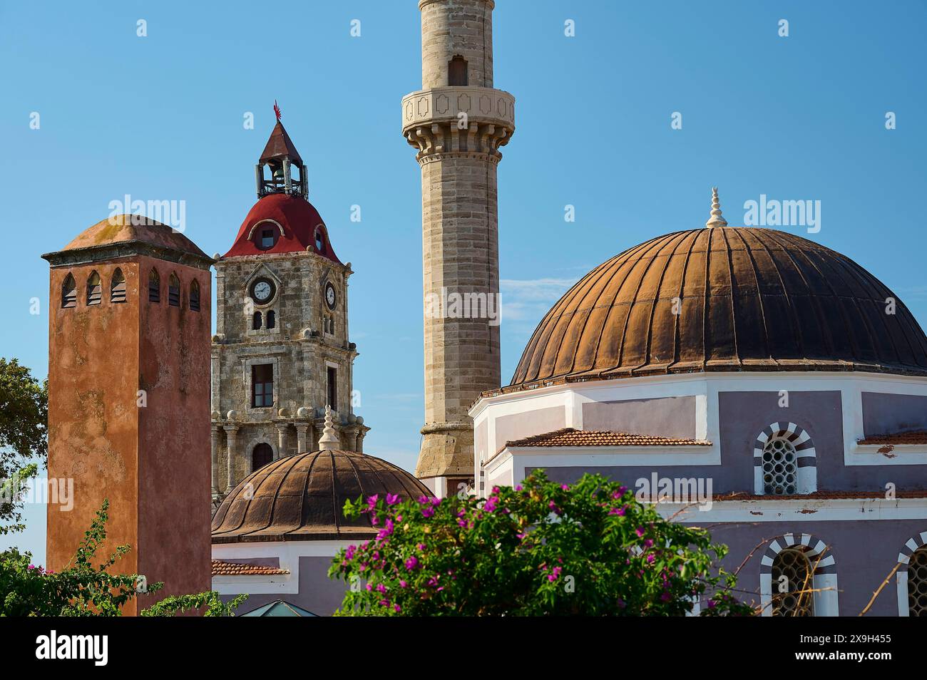 Moschea Solimana, minareto e cupole accanto al campanile con mattoni rossi, circondato da fiori e architettura storica, la città vecchia di Rodi e Rodi Foto Stock