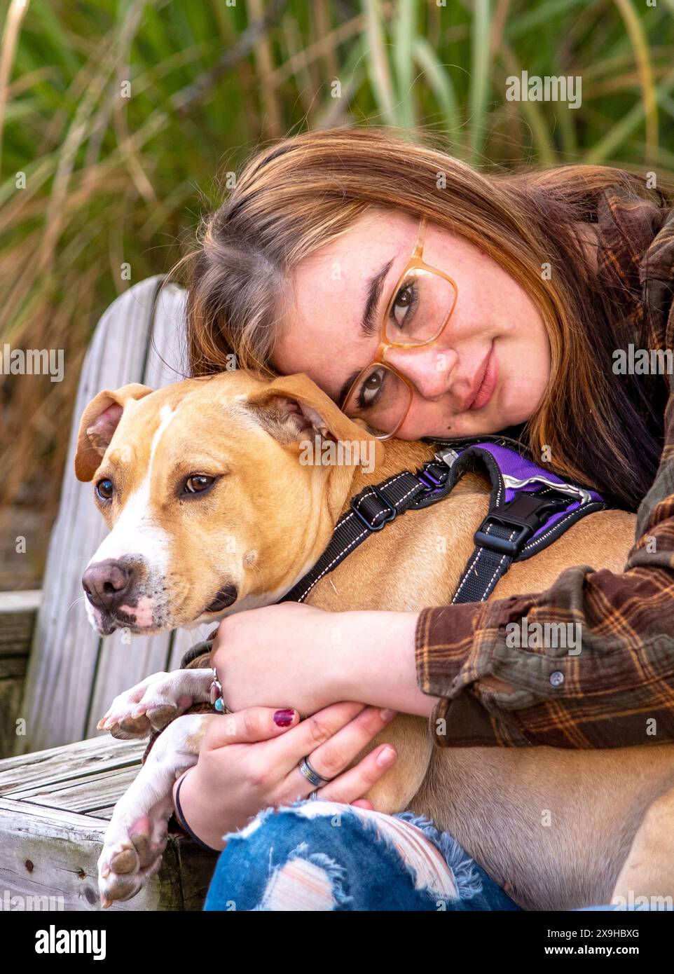 Una bella giovane donna si coccola con il suo cane da servizio in questo ritratto all'aperto Foto Stock