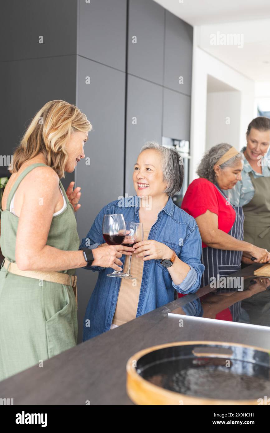 Diverse amiche anziane che tengono in mano bicchieri da vino e sorridono a casa Foto Stock