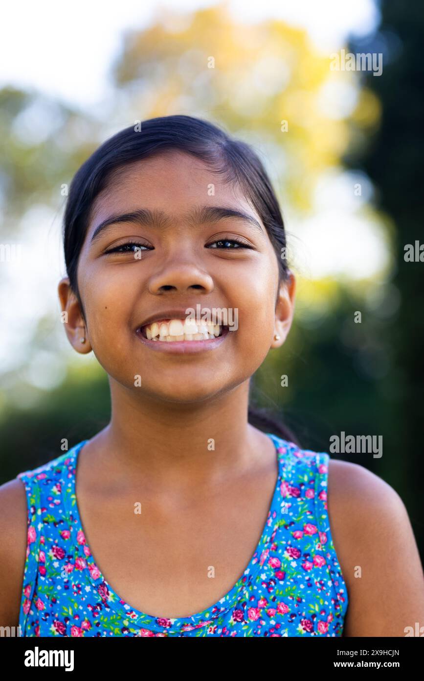 All'aperto, giovane ragazza birazziale che sorride brillantemente, indossa un colorato abito floreale Foto Stock