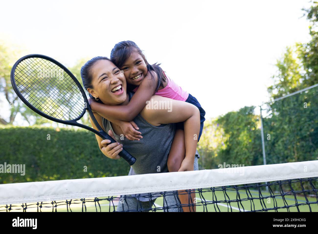 All'aperto madre e figlia birazziali sorridono con racchette da tennis sul campo da tennis Foto Stock
