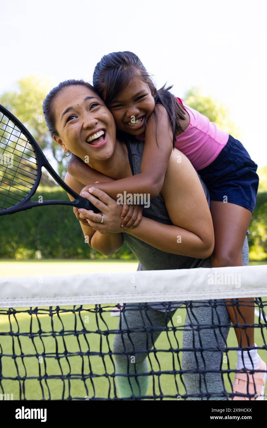 All'aperto madre e figlia birazziali sorridono con racchette da tennis sul campo Foto Stock