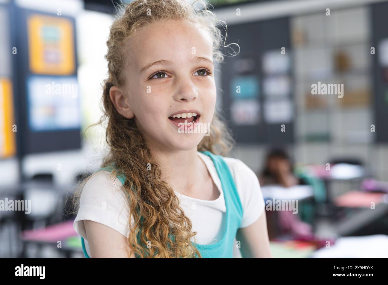 Ragazza caucasica con capelli biondi ricci sorride in un'aula scolastica Foto Stock