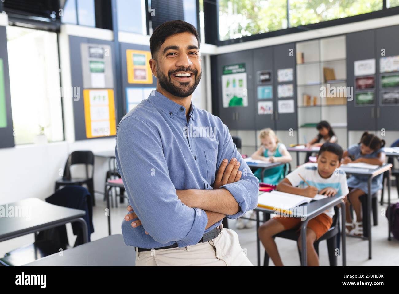 A scuola, l'insegnante maschile asiatico sorride con le braccia incrociate in classe Foto Stock
