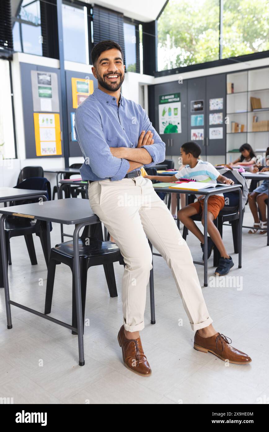 Insegnante asiatico maschile in camicia blu e pantaloni abbronzati sorride, in piedi in classe Foto Stock