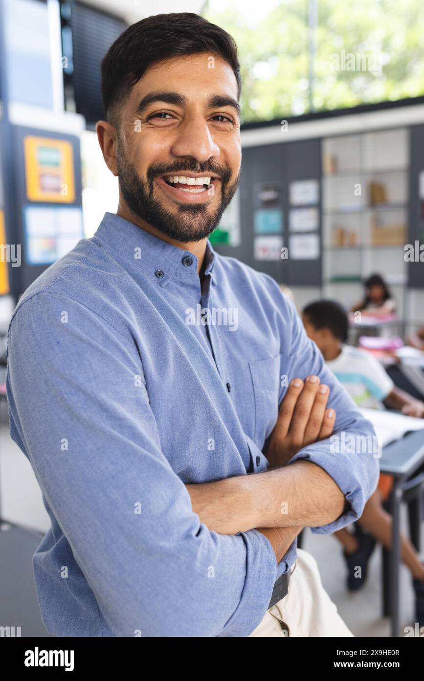 Giovane insegnante asiatico con la barba sorride con fiducia in una classe scolastica Foto Stock
