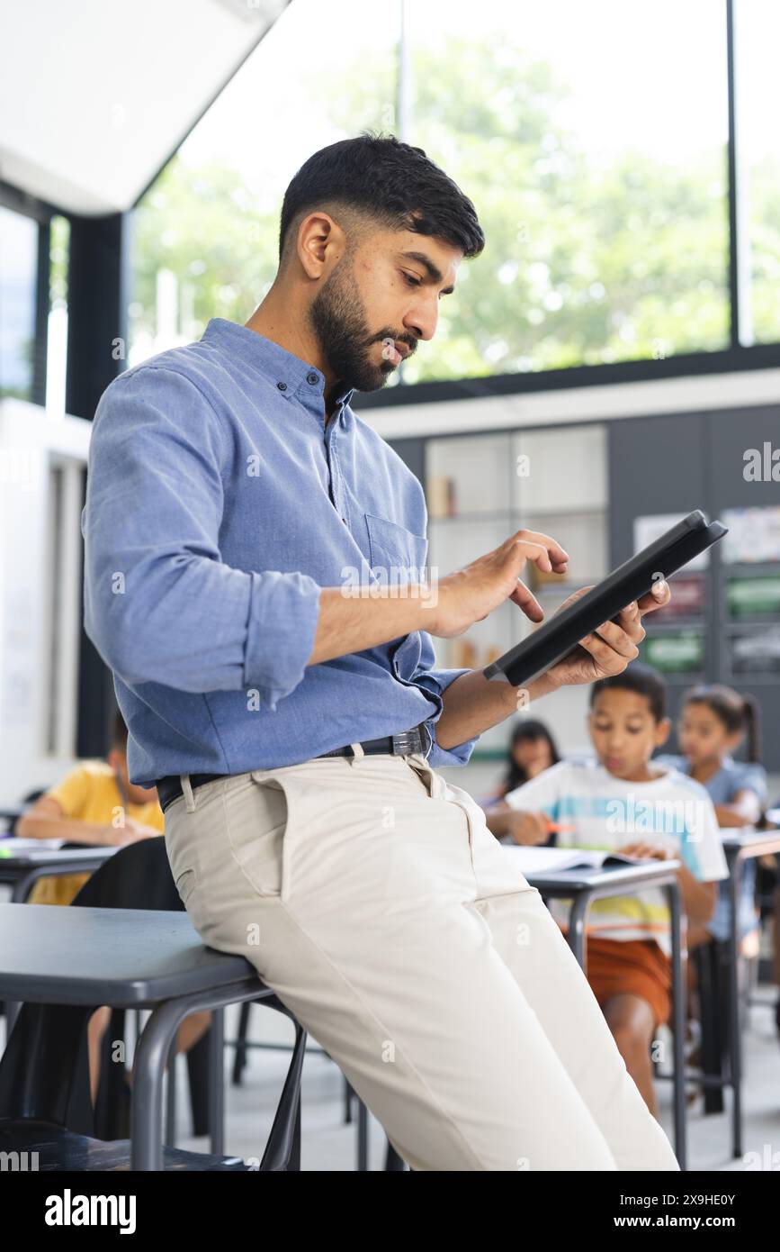Il giovane insegnante asiatico con una camicia blu si concentra su un tablet in una classe scolastica Foto Stock