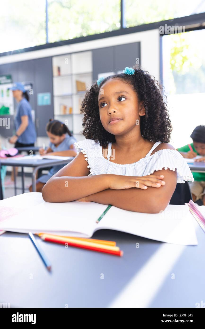 Una ragazza birazziale con i capelli ricci siede alla scrivania, profondamente nel pensiero Foto Stock