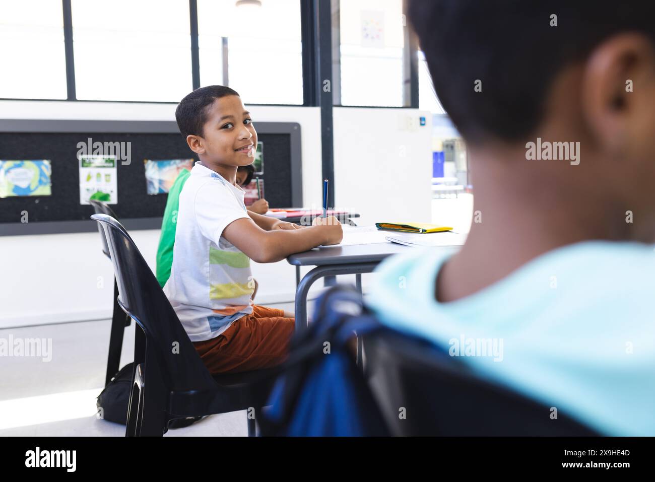 A scuola, due ragazzi birazziali sono seduti alle scrivanie, a guardarsi Foto Stock