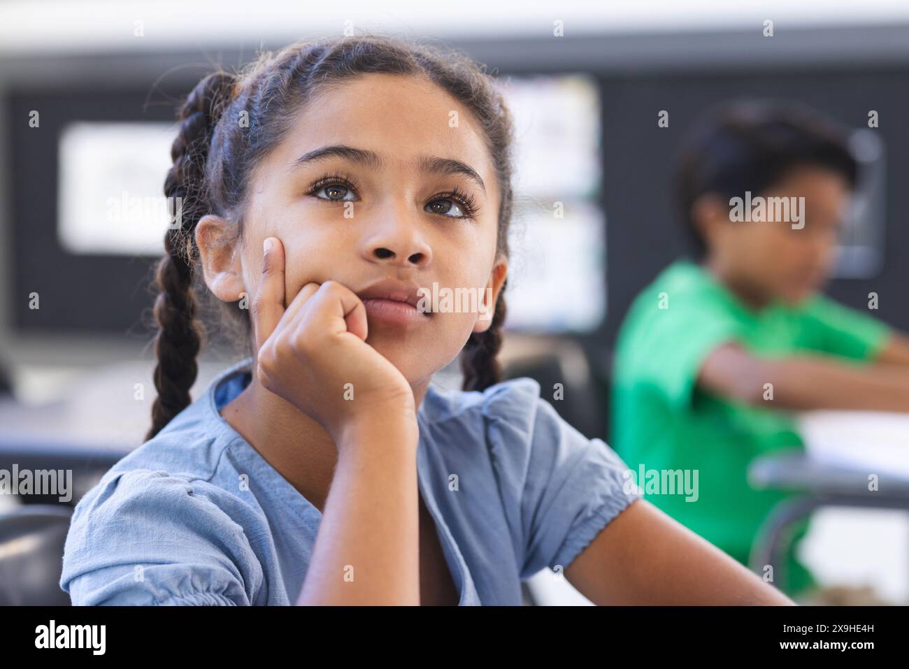 A scuola, giovane studentessa birazziale che pensa, un altro che studia dietro di lei Foto Stock