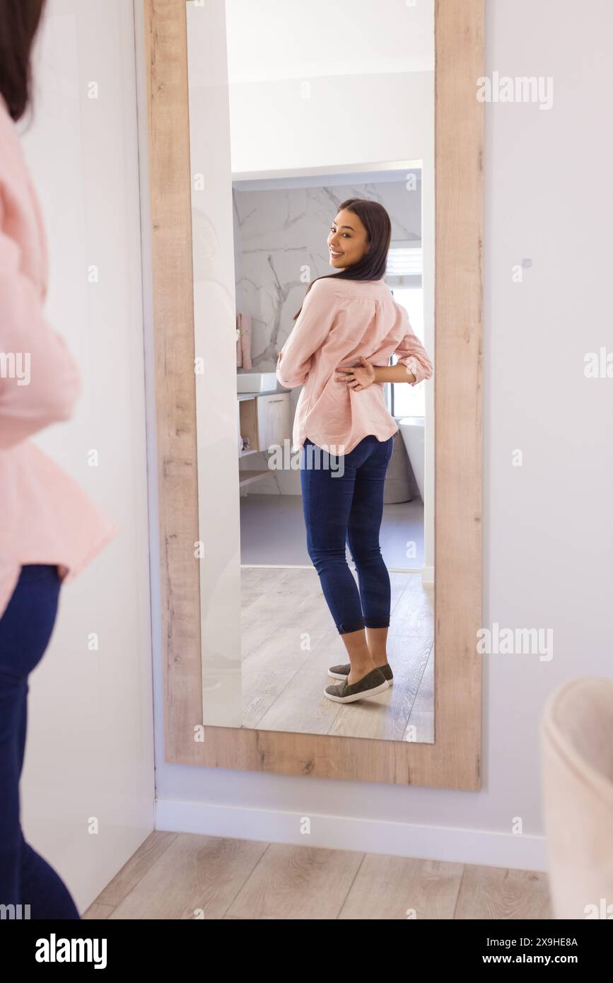 Una giovane donna birazziale che indossa jeans e top rosa, in piedi a casa Foto Stock