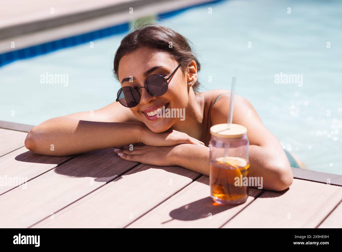 Una giovane donna birazziale che indossa occhiali da sole e si rilassa all'aperto a bordo piscina Foto Stock
