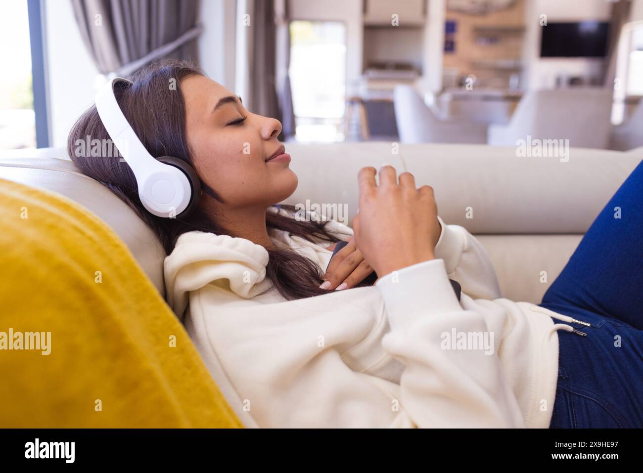 Una giovane donna birazziale che indossa le cuffie e si rilassa a casa Foto Stock