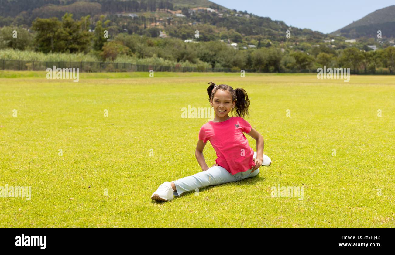 Una ragazza birazziale con trecce è seduta sull'erba in un parco con spazio per fotocopie Foto Stock