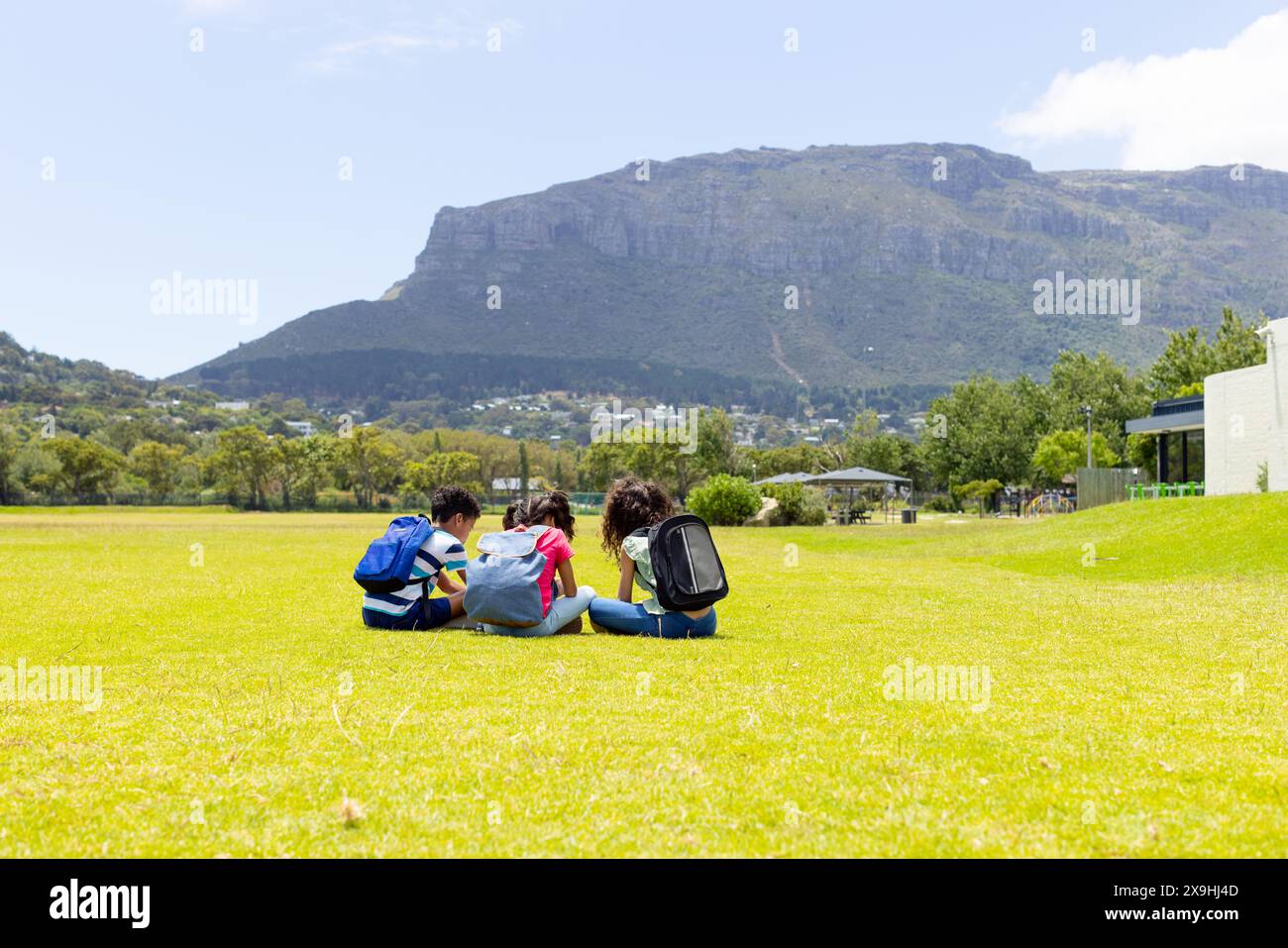 Tre studenti sono seduti sull'erba, studiano con una montagna sullo sfondo Foto Stock