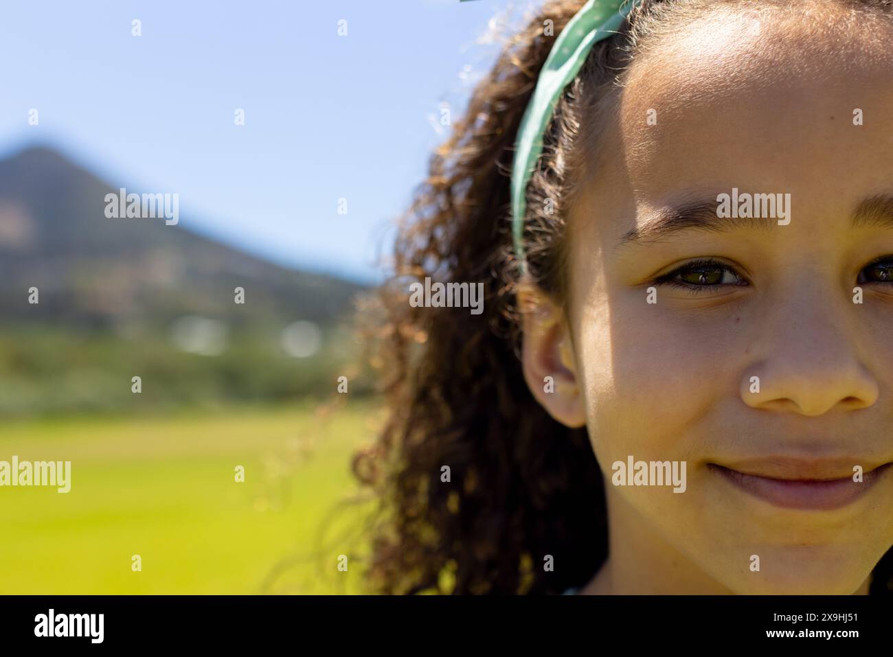 Ragazza birazziale con capelli ricci sorride all'aperto con spazio per copiare, fascia verde nei capelli Foto Stock