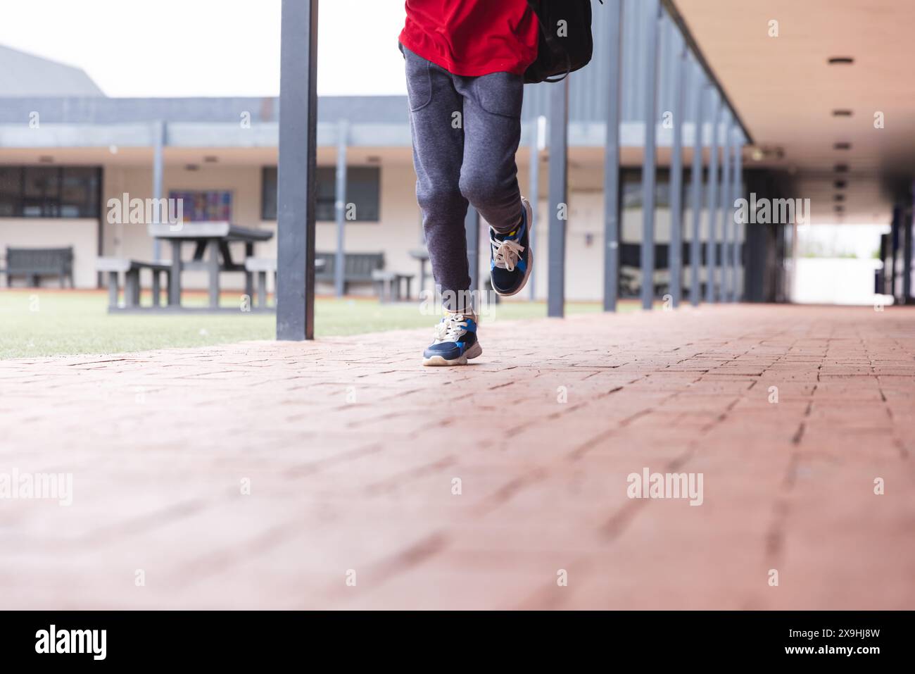 A scuola, il giovane studente birazziale maschile che indossa scarpe da ginnastica cammina all'aperto Foto Stock
