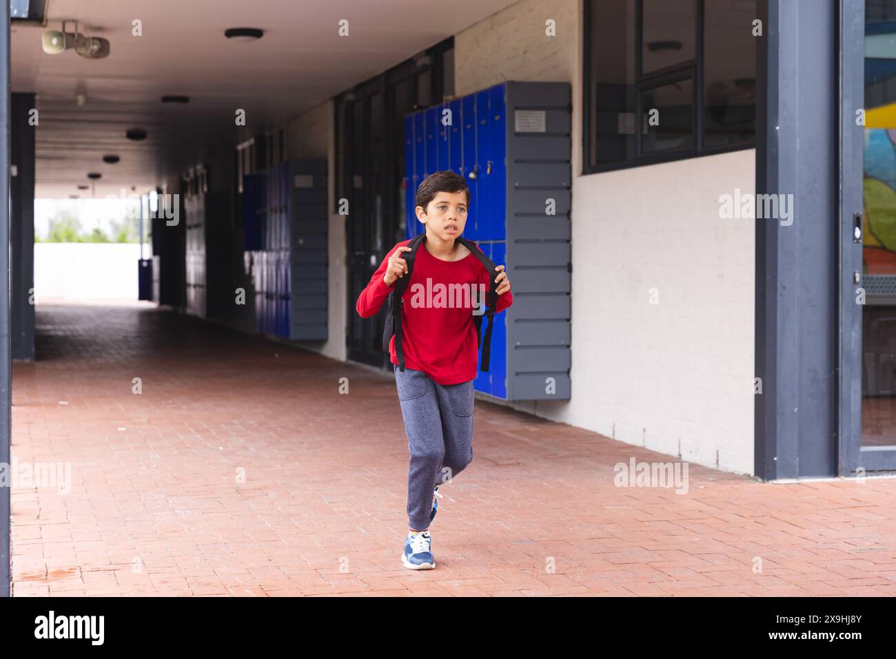 A scuola, un giovane studente birazziale maschile che indossa una camicia rossa corre all'aperto Foto Stock