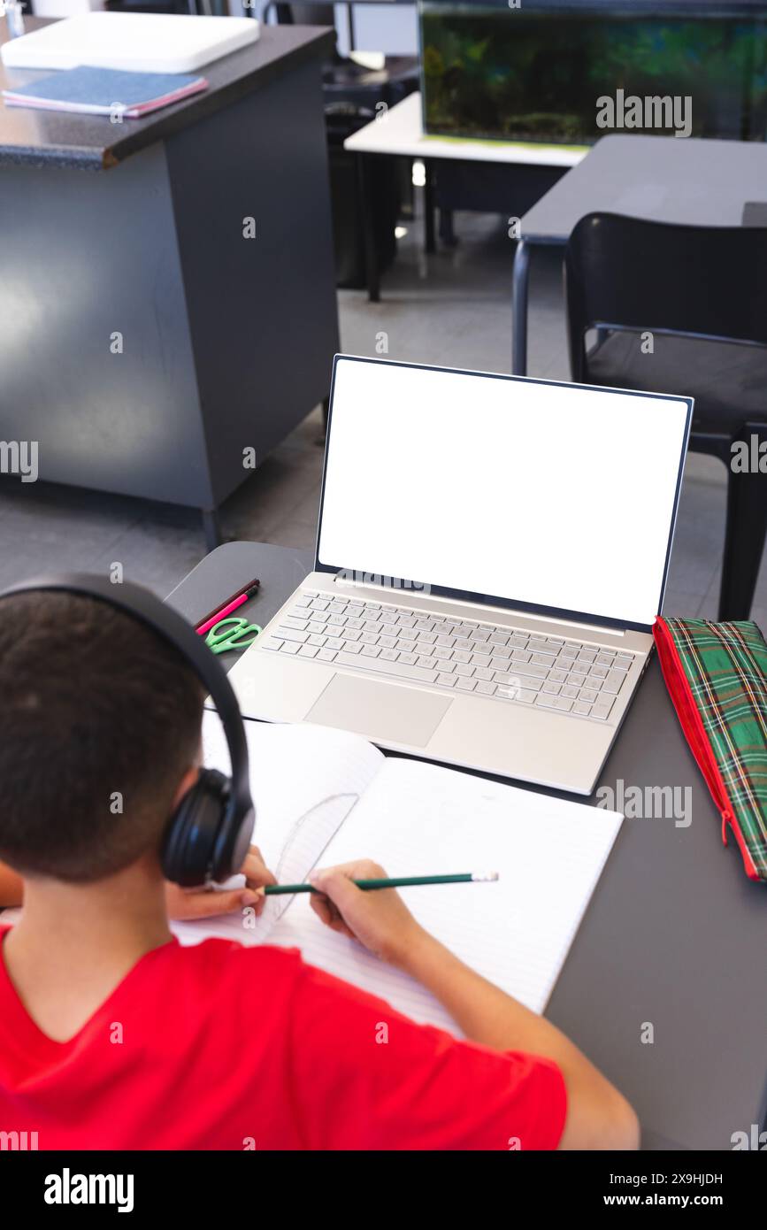 Un ragazzo birazziale studia in una classe scolastica usando un laptop, con spazio per le copie Foto Stock