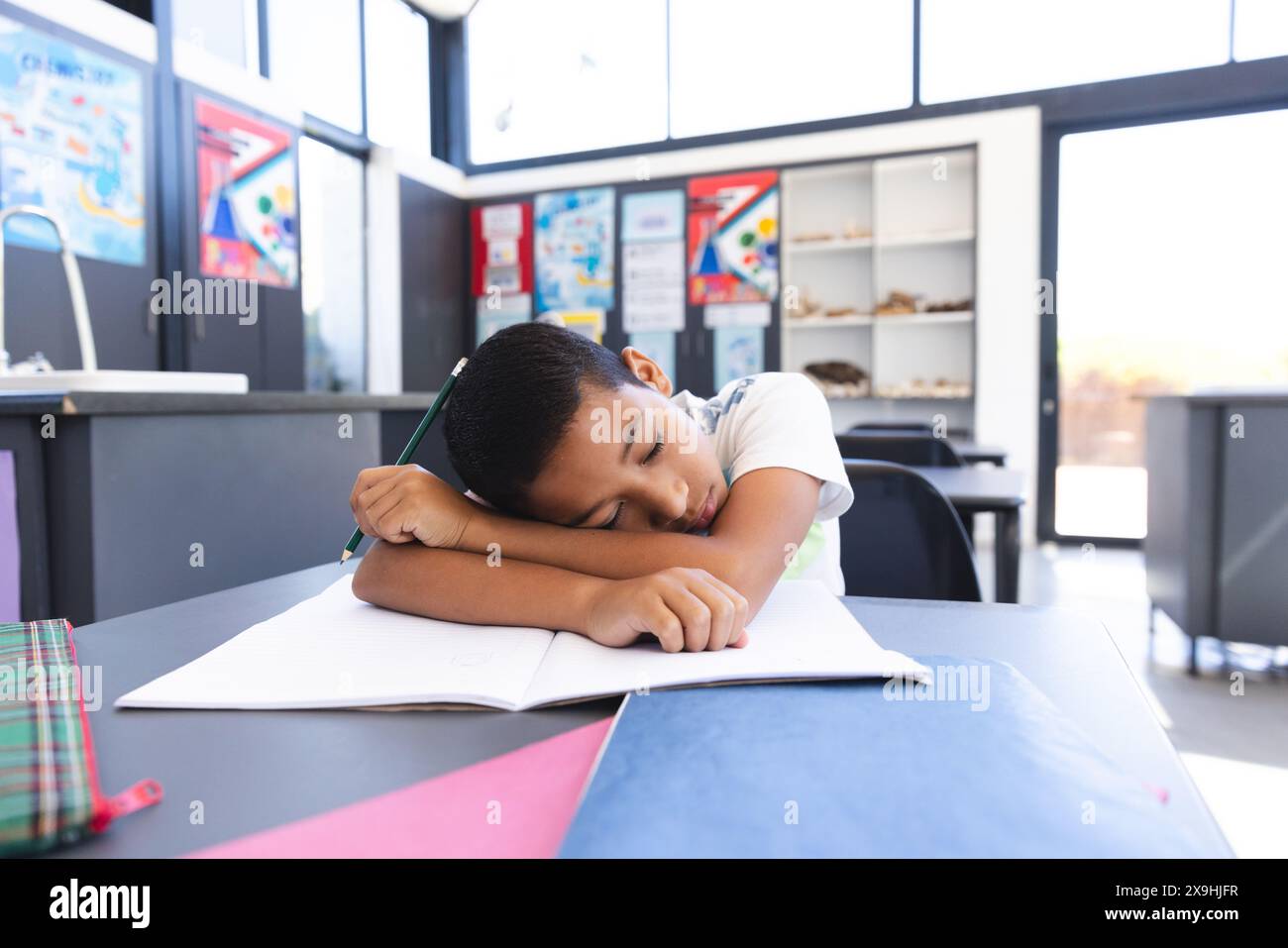Il ragazzo birazziale esausto riposa sulla scrivania durante gli studi in una luminosa aula. Foto Stock