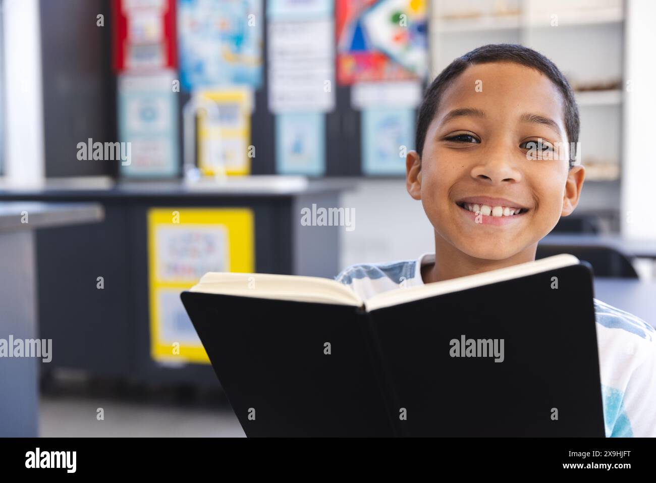 Un ragazzo birazziale ama leggere un libro in classe a scuola Foto Stock