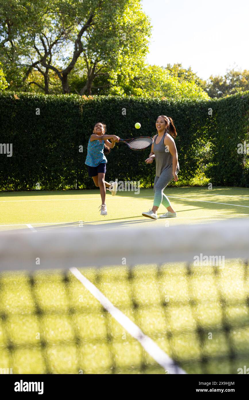 All'aperto, madre e figlia birazziali giocano a tennis insieme su un campo Foto Stock