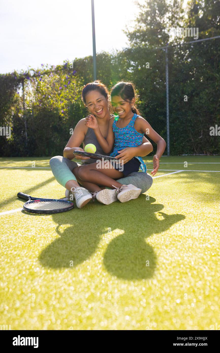 All'aperto, madre e figlia birazziali sorridono sul campo da tennis con racchette da tennis Foto Stock