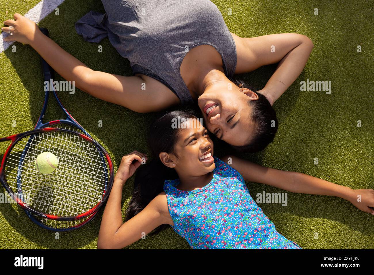 All'aperto madre e figlia birazziali sdraiate sull'erba con racchette da tennis, sorridenti Foto Stock