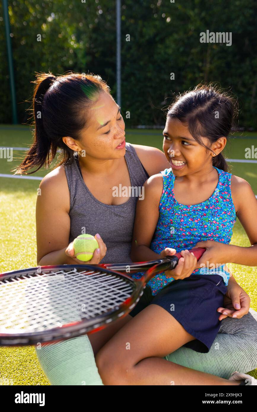 Madre e figlia birazziali si divertono a tennis insieme all'aperto, tenendo racchetta e palla Foto Stock