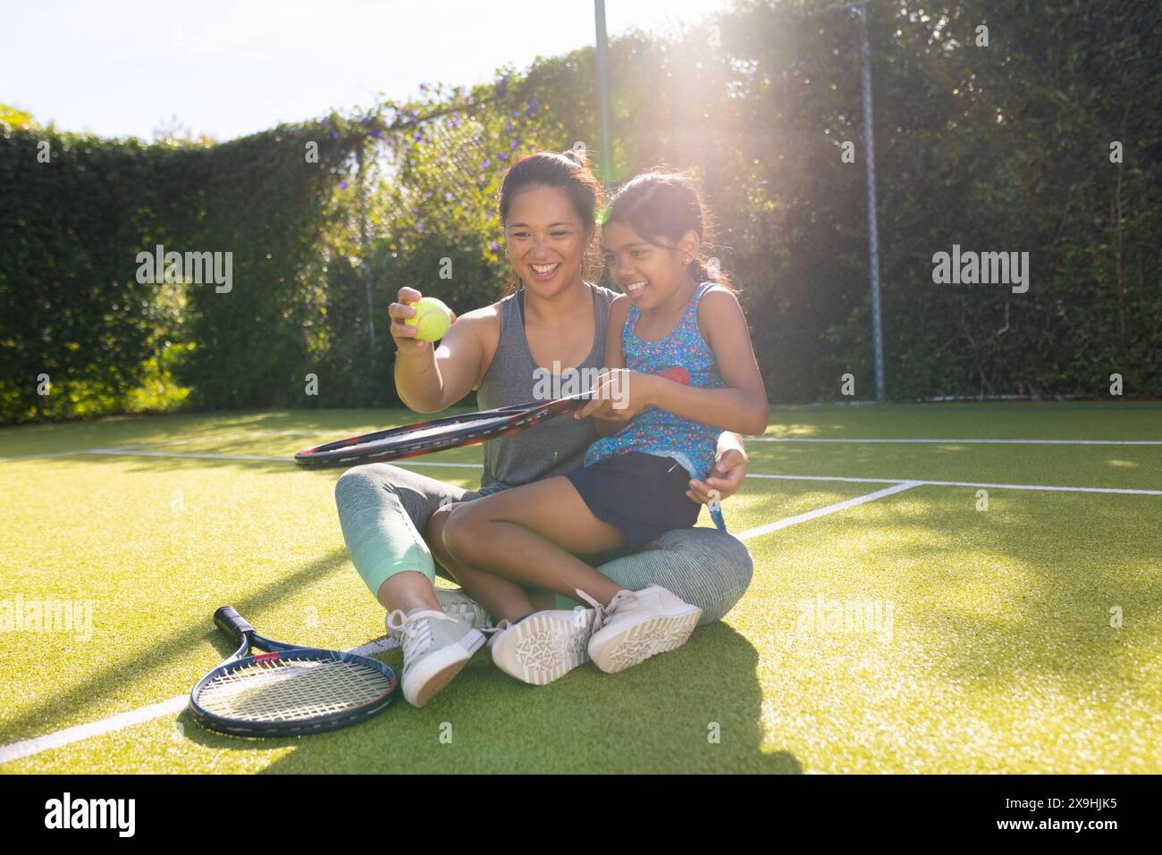 Madre e figlia birazziali sorridenti, giocano a tennis all'aperto con le loro racchette Foto Stock