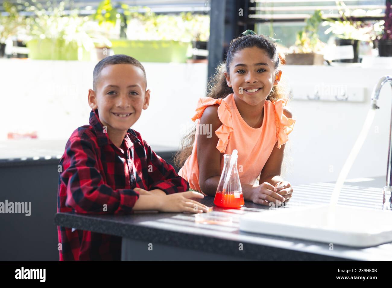 Ragazzo e ragazza birazziali si impegnano in un esperimento scientifico a scuola, sorridendo alla telecamera Foto Stock