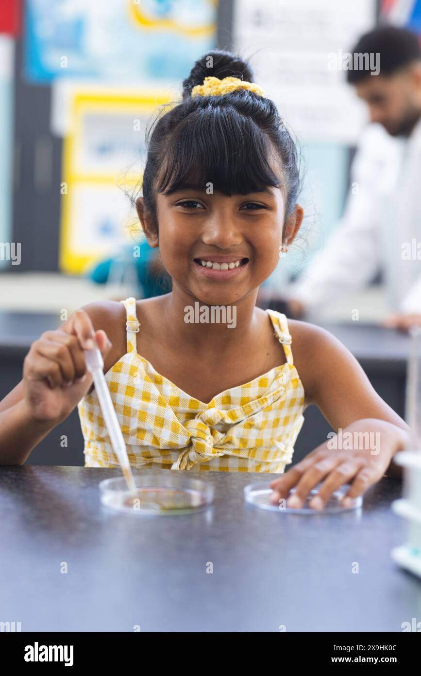 Una ragazza birazziale con un vestito giallo conduce un esperimento scientifico a scuola Foto Stock