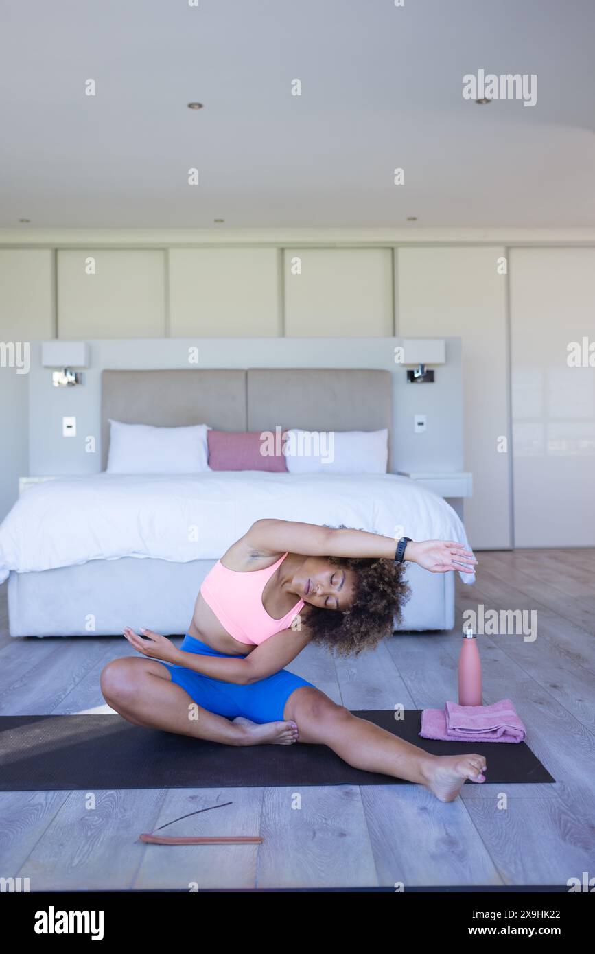 A casa, giovane donna birazziale che si allunga su un tappetino da yoga Foto Stock