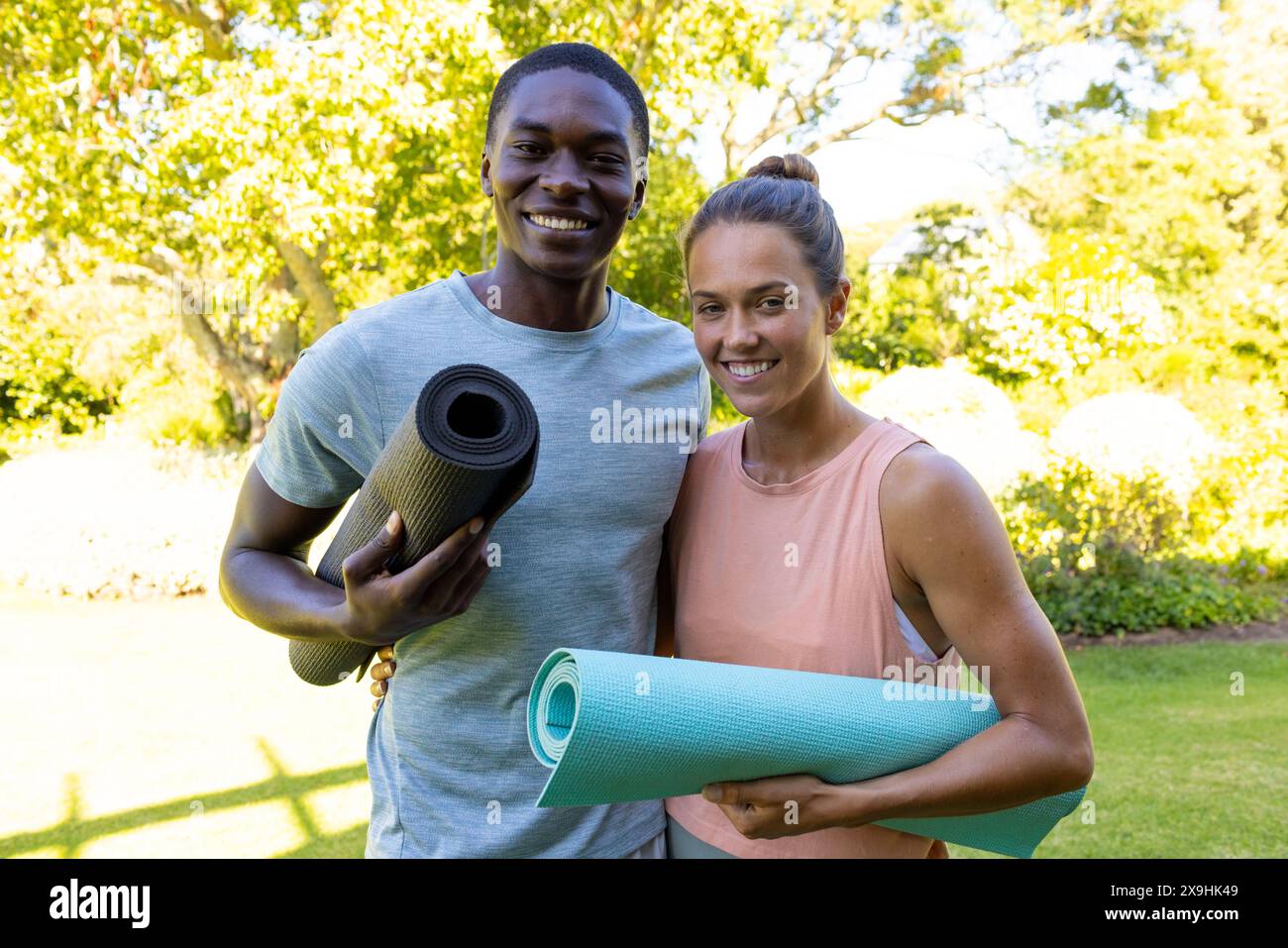 Una coppia giovane e variegata che tiene stuoie per lo yoga, sorridendo all'aperto Foto Stock