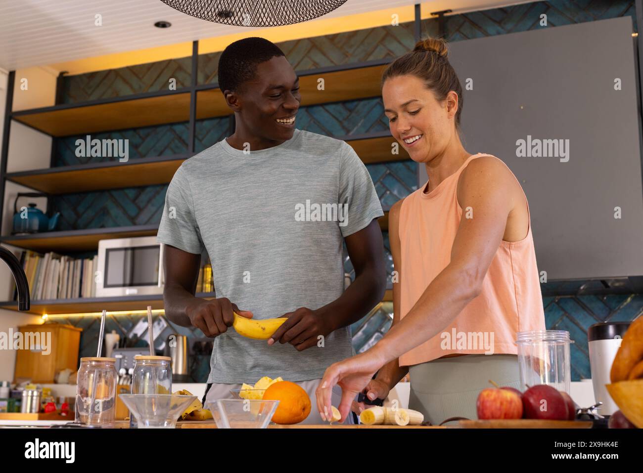 Una coppia variegata a casa che prepara frutta, sorridendo l'un l'altra Foto Stock Una coppia variegata a casa che prepara frutta, sorridendo l'un l'altra Foto Stock
