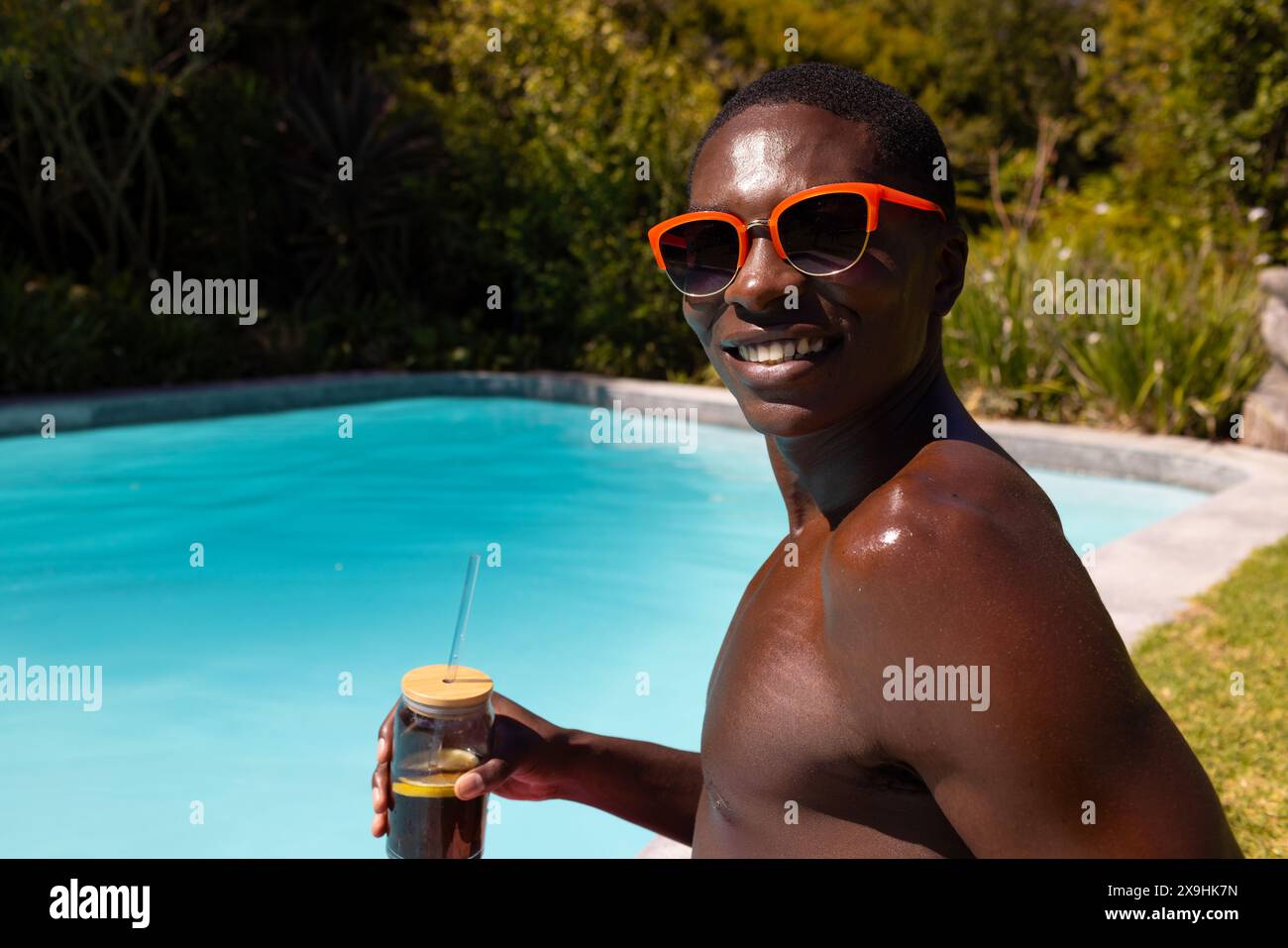 Un giovane afroamericano fuori, che tiene un drink a bordo piscina Foto Stock Un giovane afroamericano fuori, che tiene un drink a bordo piscina Foto Stock