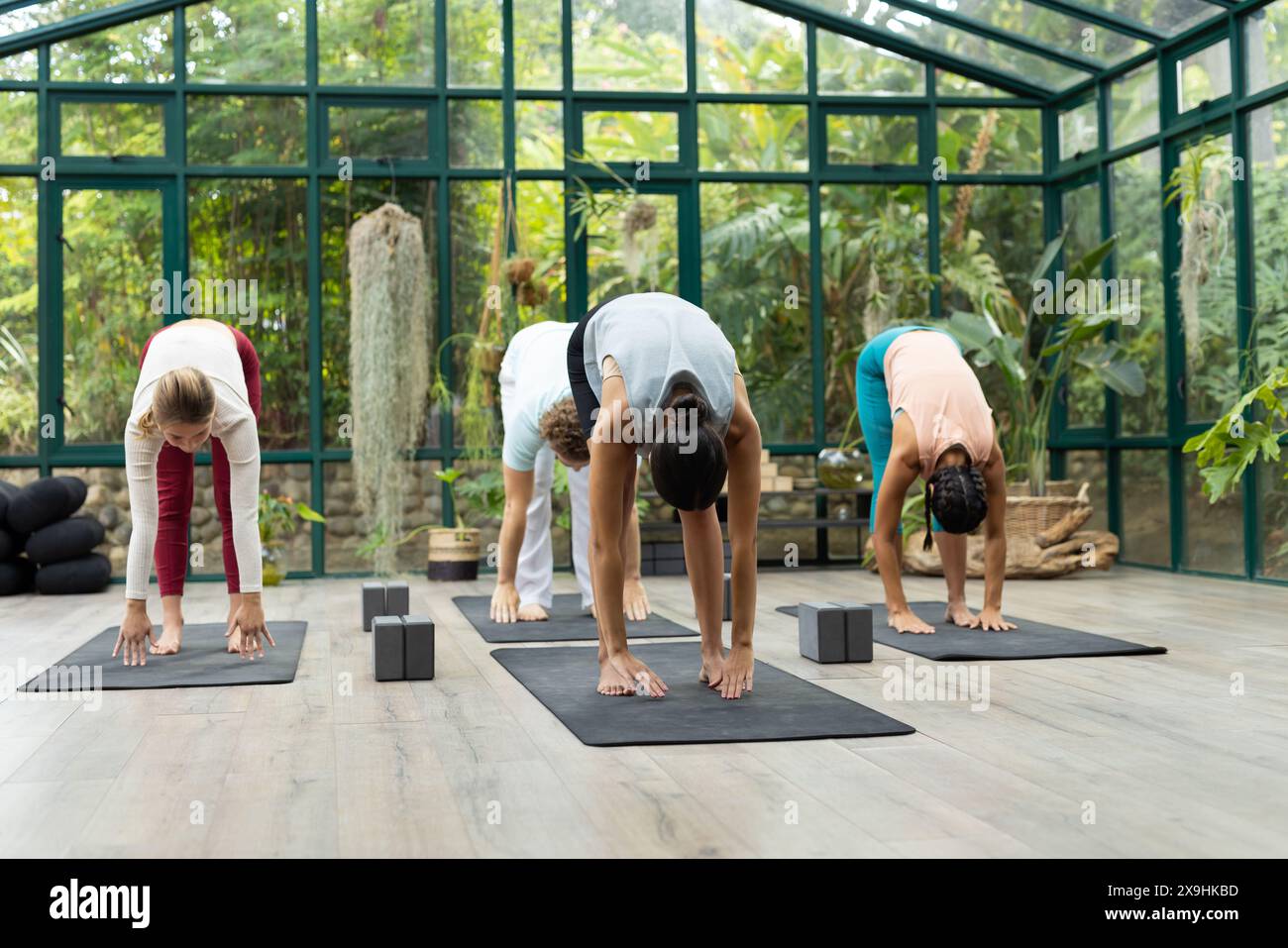 Diversi studenti di yoga e insegnanti di Pacific Islander si piegano sui tappetini al Glass House Studio Foto Stock