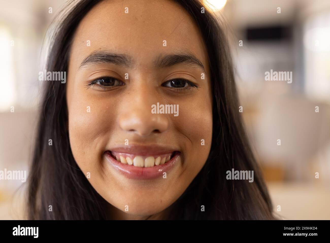 Una giovane ragazza birazziale con lunghi capelli castani scuri, sorridente a casa Foto Stock