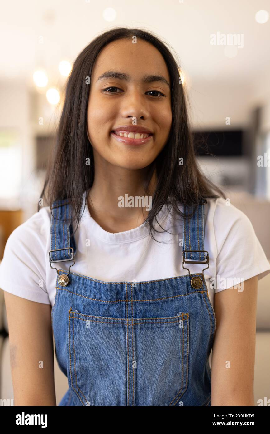 Una giovane ragazza birazziale che indossa una tuta in denim e sorride a casa Foto Stock