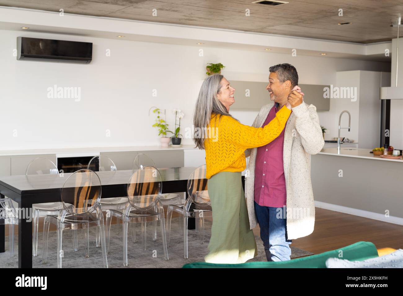 A casa, diverse coppie senior che ballano insieme in una cucina moderna, sorridono, spazio copia. Marito birazziale con capelli grigi corti e moglie caucasica con Foto Stock