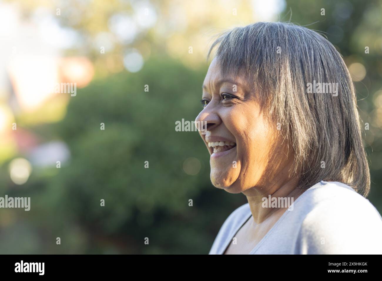 All'aperto, donna birazziale anziana sorridente in un giardino lussureggiante con alberi, spazio fotocopie Foto Stock