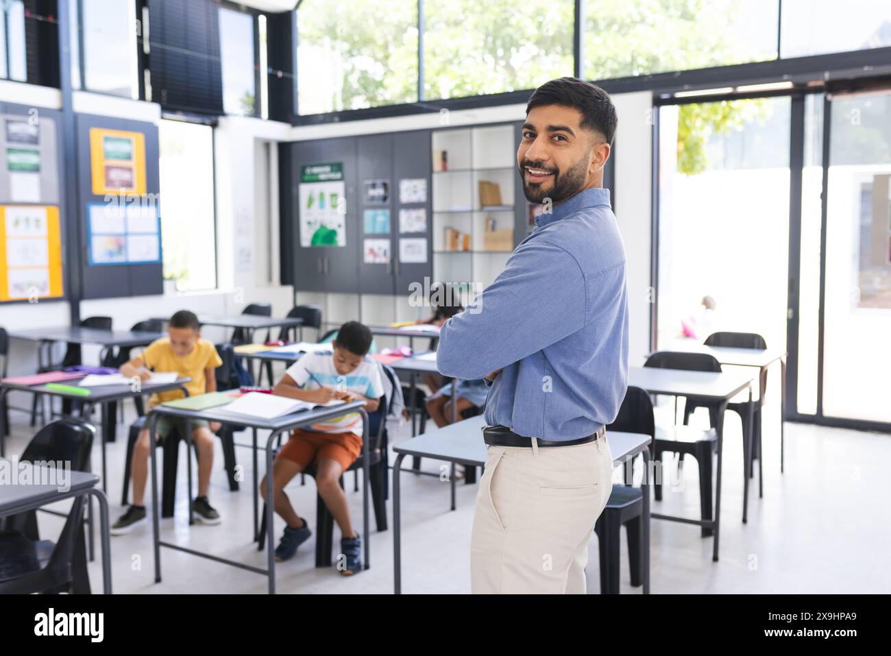 A scuola, l'insegnante maschile asiatico sorride in classe, gli studenti si concentrano sul lavoro Foto Stock