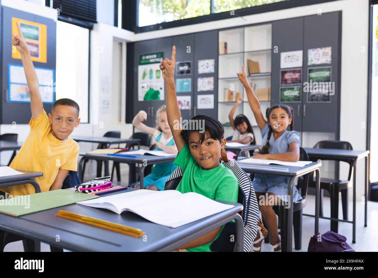 Bambini che alzano le mani con impazienza in una classe scolastica Foto Stock