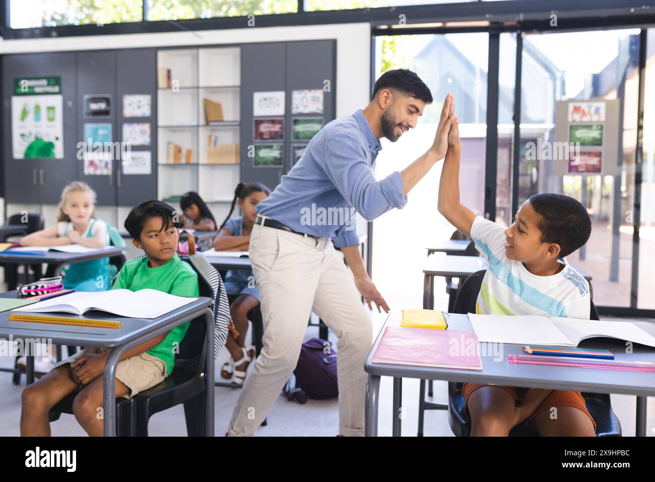 L'insegnante si congratula con un ragazzo birazziale con un cinque in una classe scolastica Foto Stock