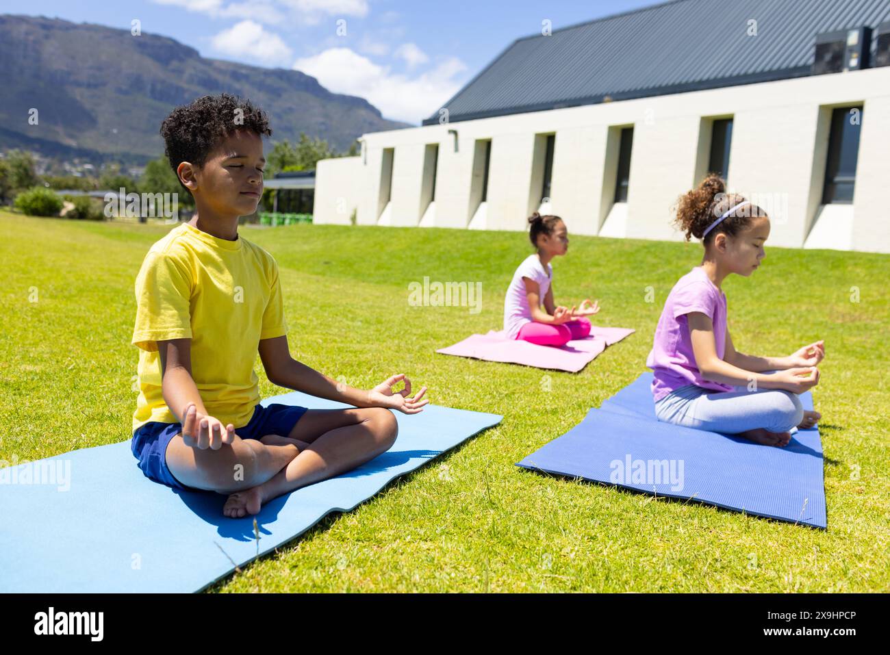 I ragazzi e le ragazze birazziali praticano yoga all'aperto su tappeti Foto Stock