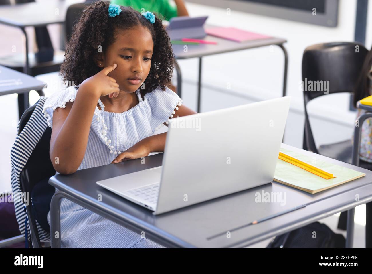 A scuola, una giovane studentessa birazziale sta guardando un portatile in classe Foto Stock