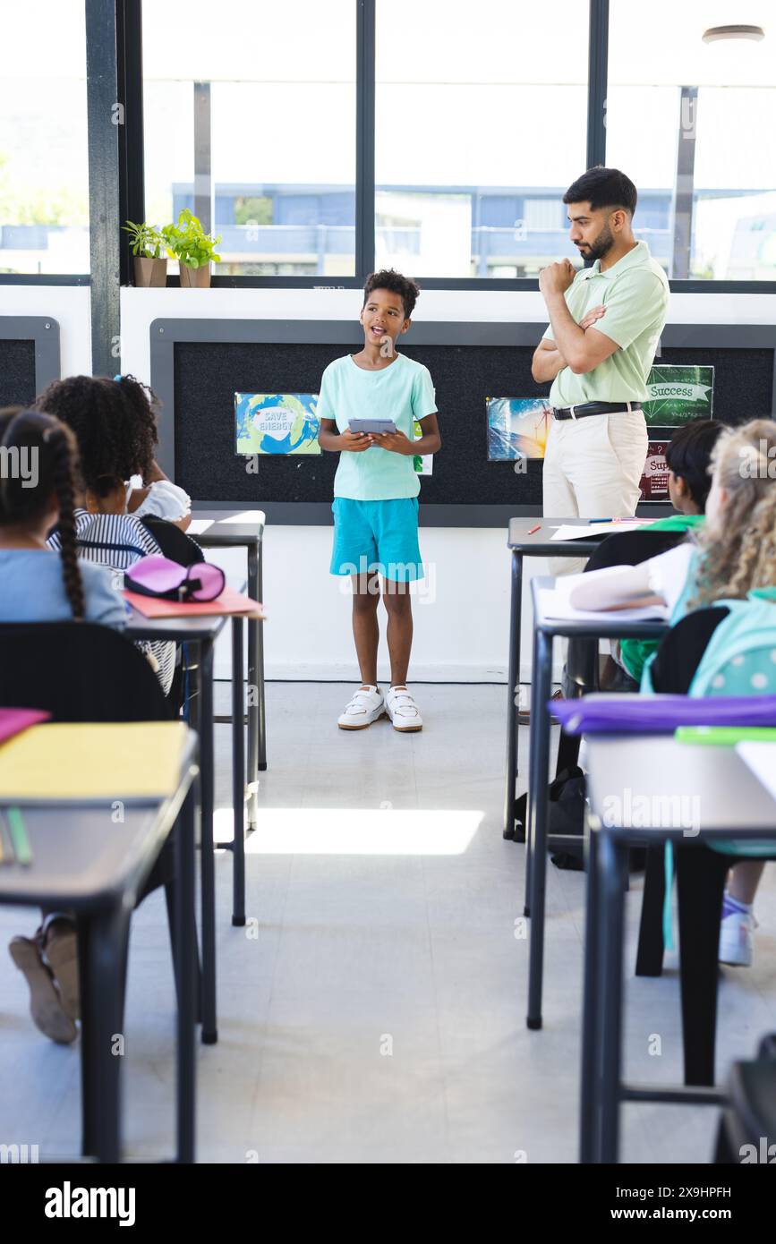 A scuola, la giovane ragazza birazziale sta presentando, con un insegnante asiatico maschile che guarda Foto Stock